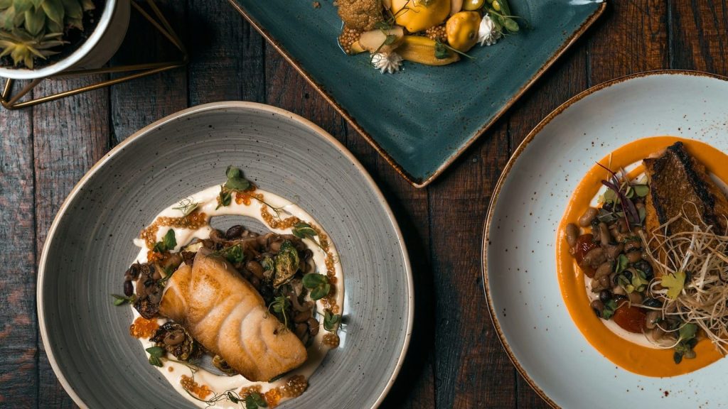 Drie verfijnde restaurantgerechten met eerlijke ingrediënten, gepresenteerd op een houten tafel.