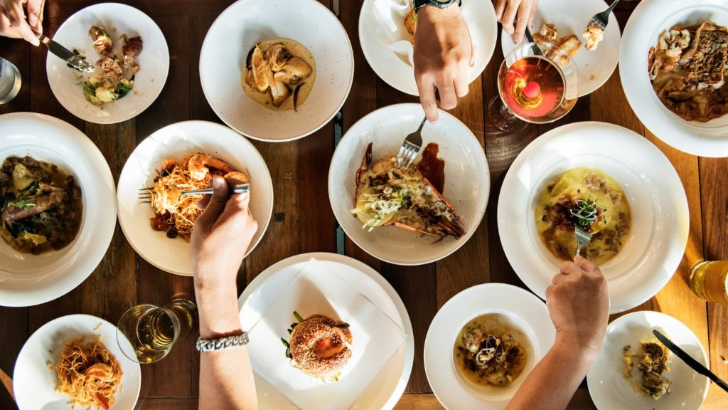 Gasten delen meerdere gerechten aan tafel als voorbeeld bij een eigen restaurant beginnen met gevarieerde menukaart