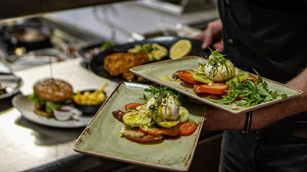 Server draagt gerechten uit tijdens piekmoment, illustratie van werkdruk horeca op de werkvloer